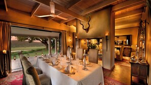 Uma área de refeições com uma mesa comprida posta para uma refeição, um candelabro e vista para o exterior.
