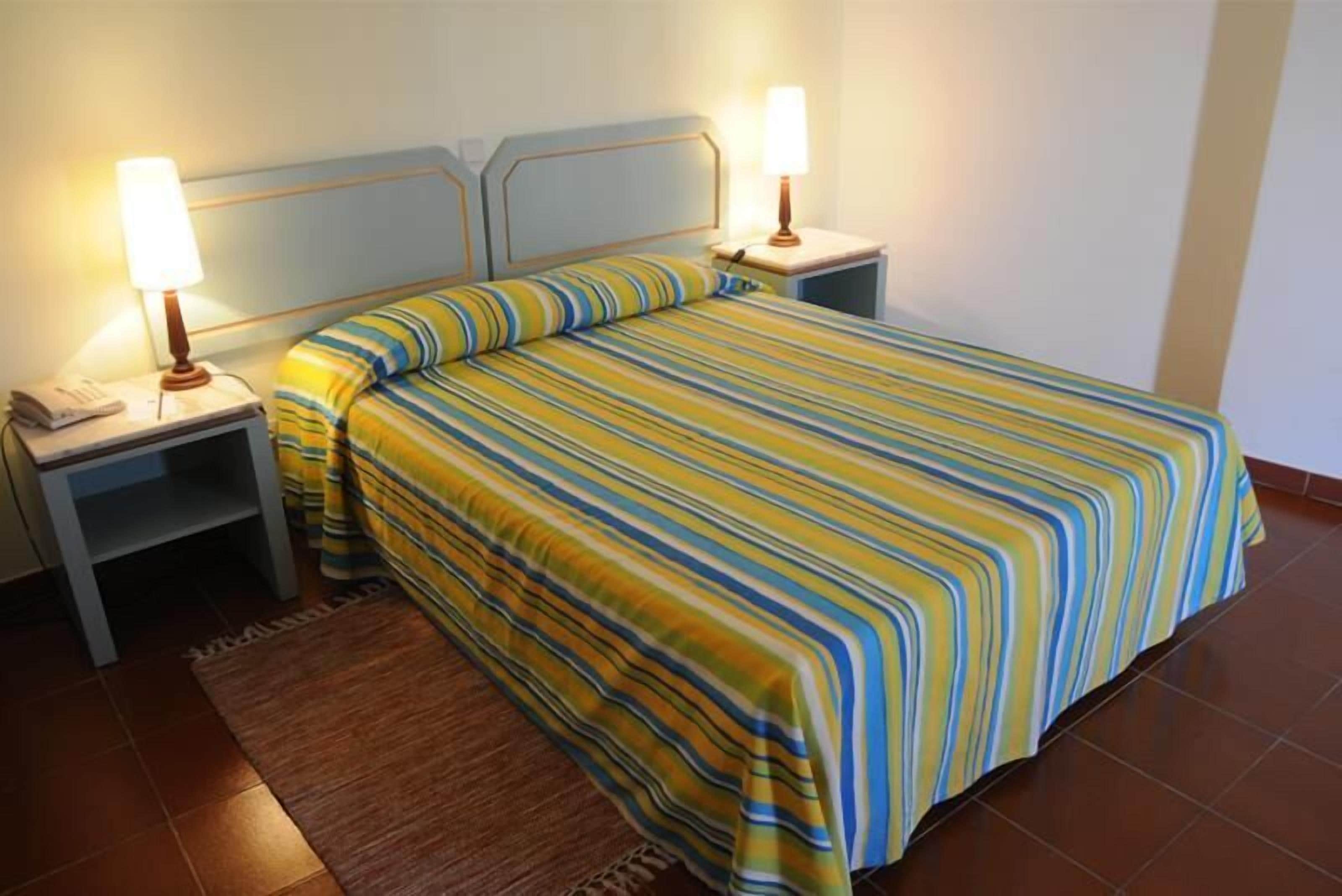 A hotel room with a bed, two bedside tables, and a nightstand.