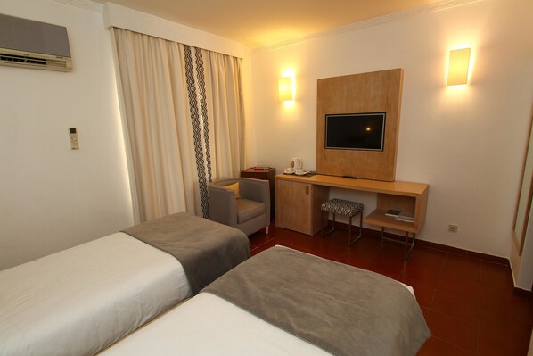 A hotel room with two single beds, a desk with a chair, a television, and a small seating area with a patterned chair. - Best Western Hotel Dom Bernardo (Faro)