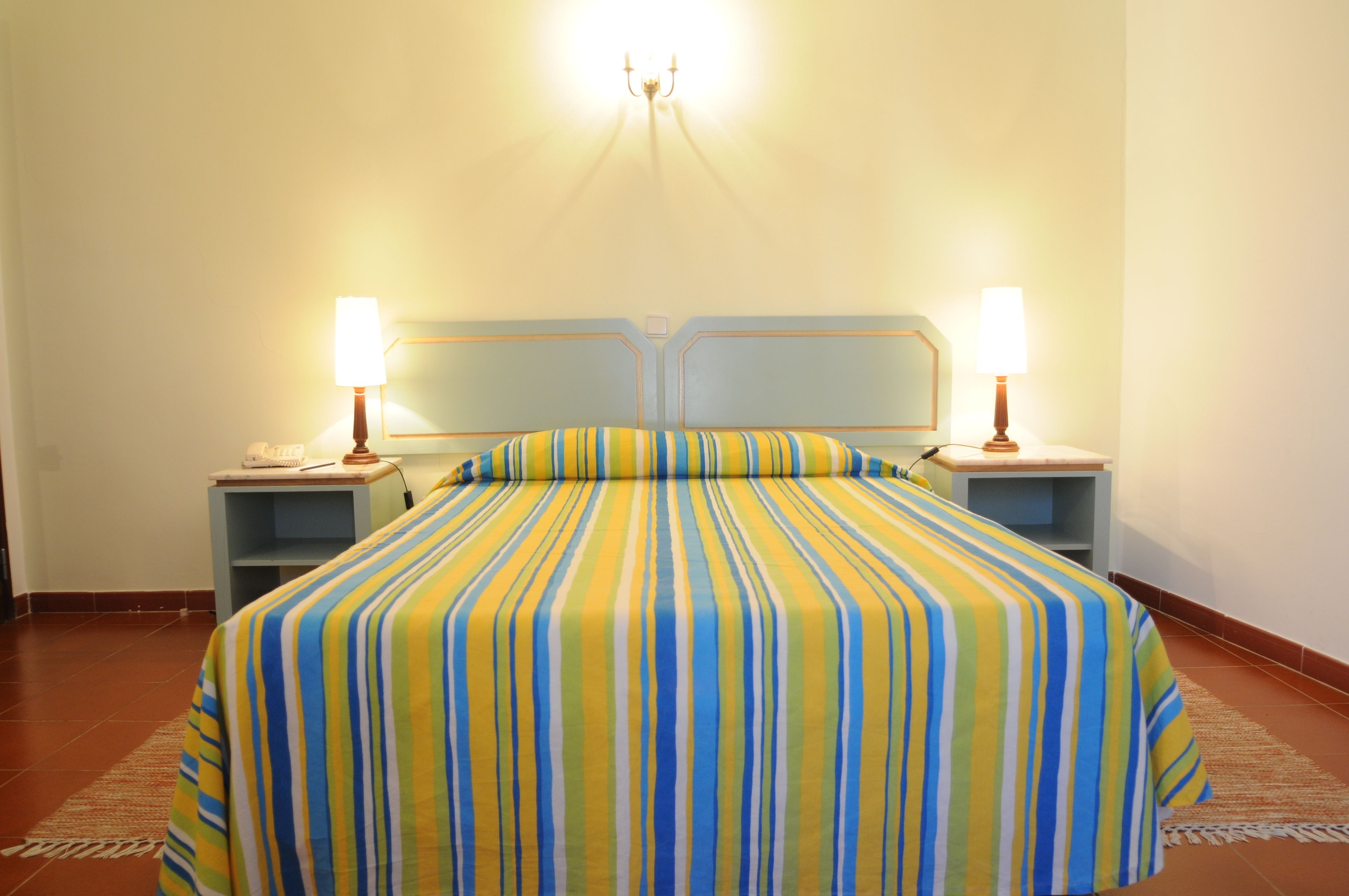 A hotel room with a large bed, two bedside tables, and a wall-mounted light fixture.