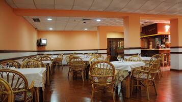 A restaurant with multiple tables and chairs, a television mounted on the wall, and a counter with a sign.