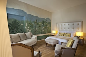 A hotel room with a large mural, a bed with a tufted headboard, a sofa, a chair, and two bedside tables with lamps. - Château de Siran (Siran)
