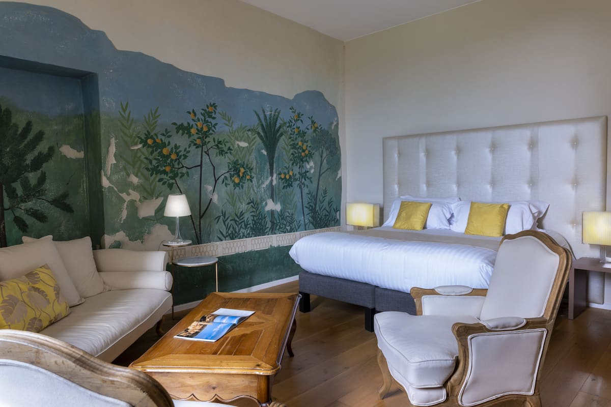 A hotel room with a bed, a sofa, a chair, a coffee table, and a mural on the wall.