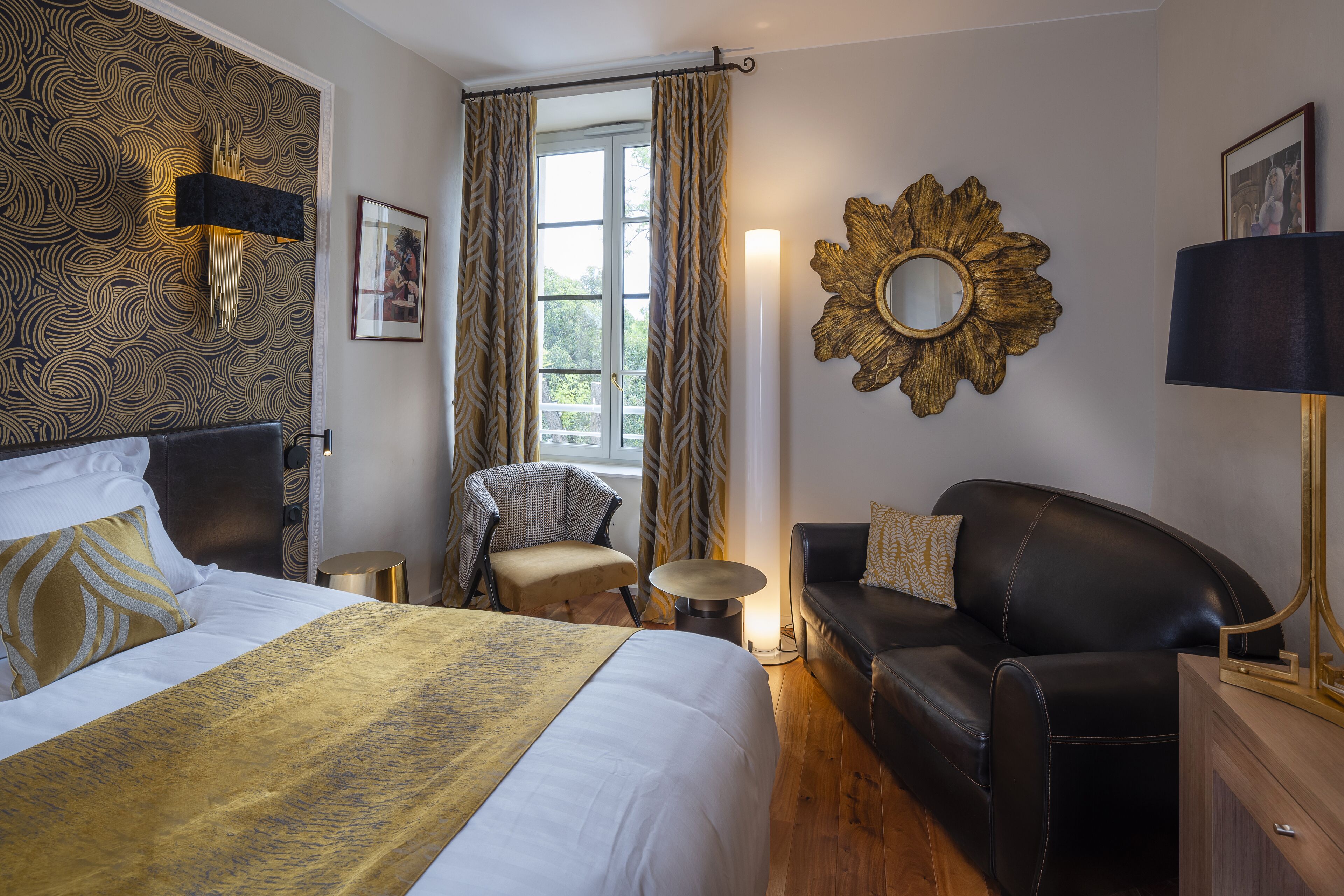 Una habitación de hotel con una cama, dos sillas, un sofá, una mesa redonda y un espejo grande en la pared.