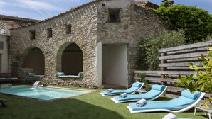 Un edificio de piedra con piscina, sillones de exterior y valla de madera.