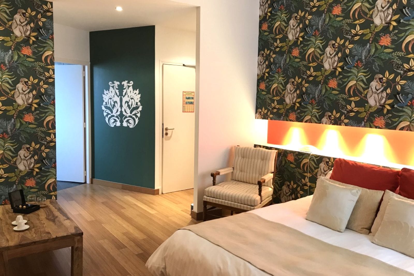 A hotel room with a bed, a chair, a table, and a wall with a floral pattern.