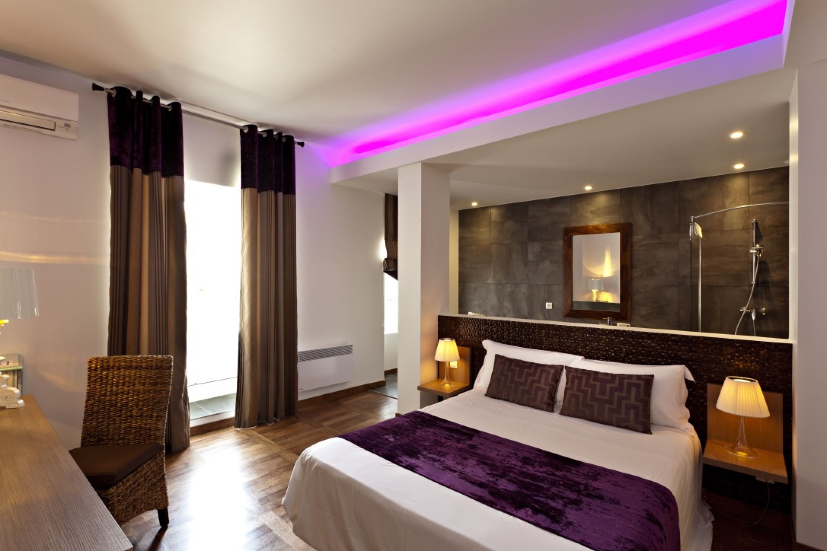 Een moderne hotelkamer met een groot bed, een spiegelheadboard, bedlampjes en uitzicht op het omliggende landschap.