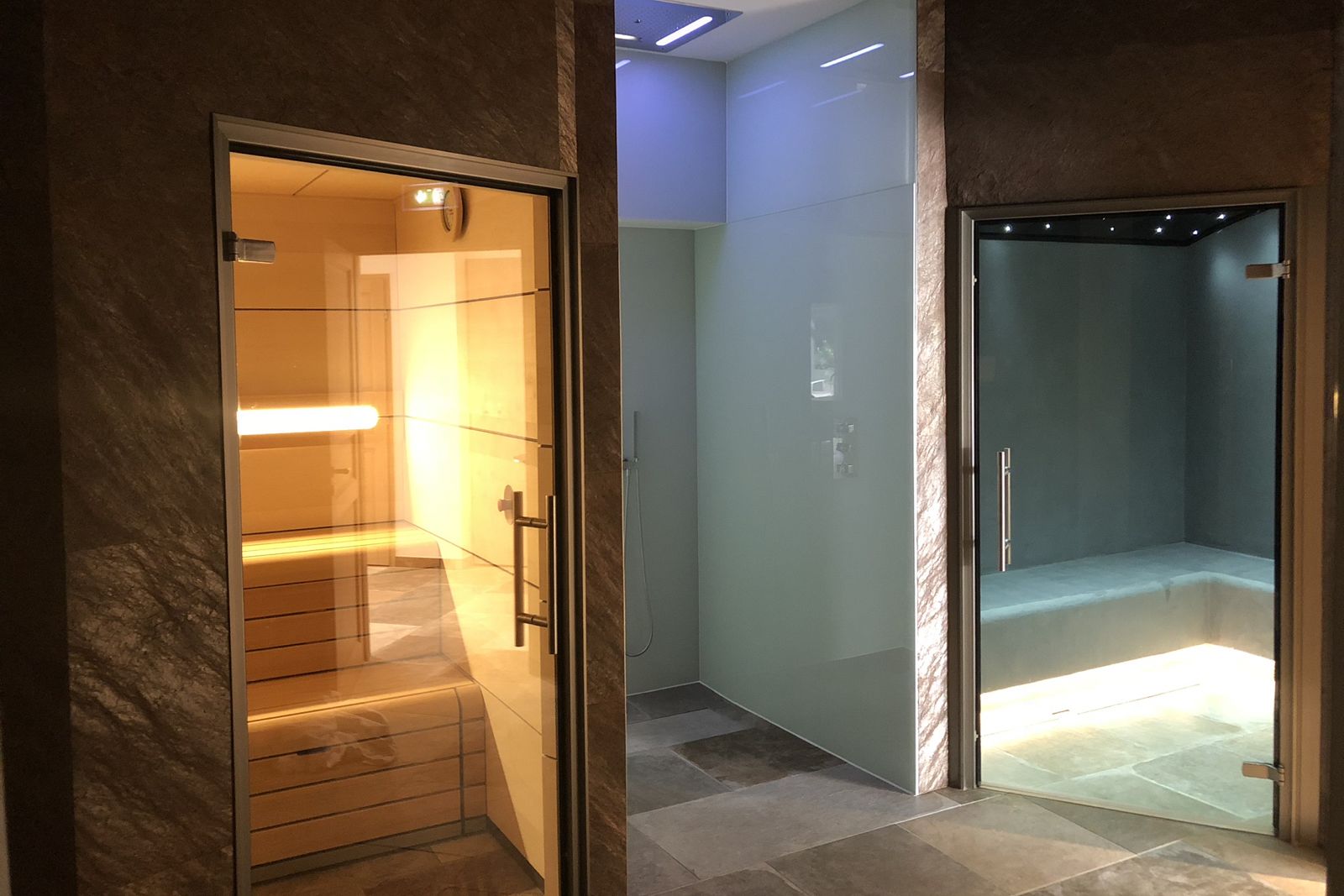 Un baño moderno con cabina de ducha de vidrio, un banco de madera y suelo de baldosas.