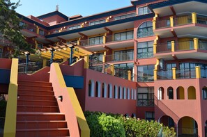 Un hotel de varios pisos con fachada roja y amarilla, múltiples balcones y una escalera que conduce a los niveles superiores.
