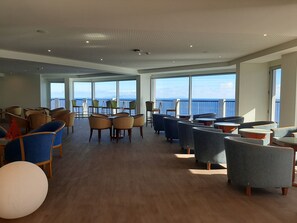 Amplia sala de estar con múltiples opciones de asientos, ventanas grandes con vista al mar y un techo alto con iluminación empotrada.