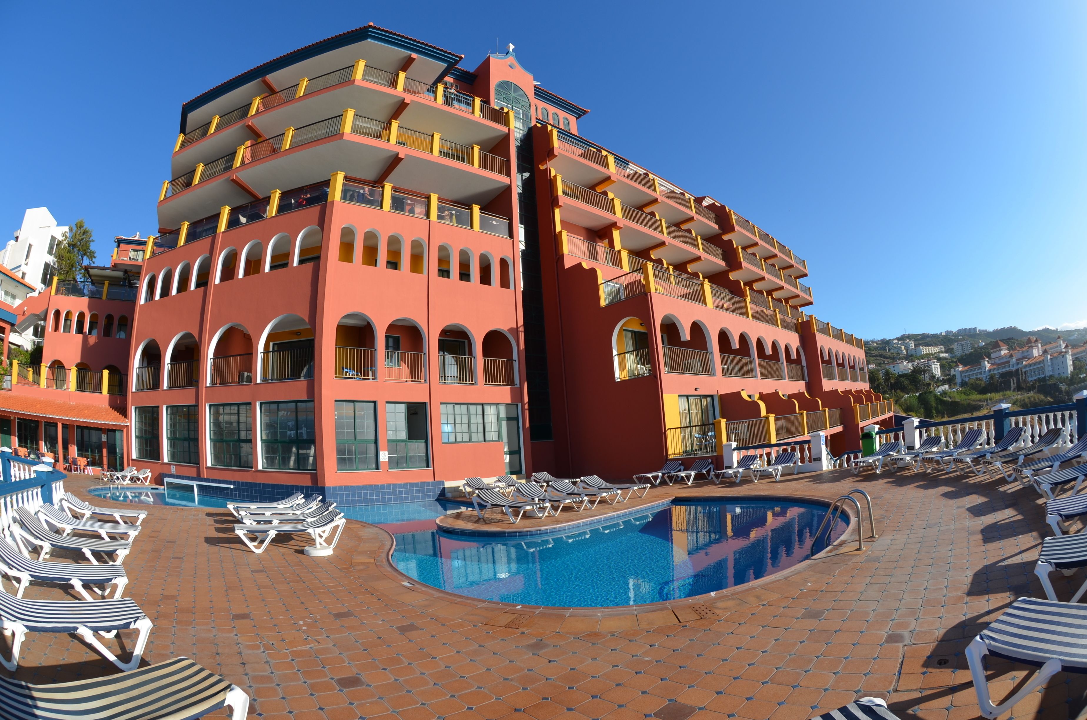 A hotel with a pool area, multiple balconies, and a clear blue sky.