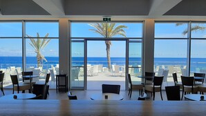A spacious indoor area with large windows offering a view of the ocean and palm trees. - Royal Orchid (Santa Cruz)