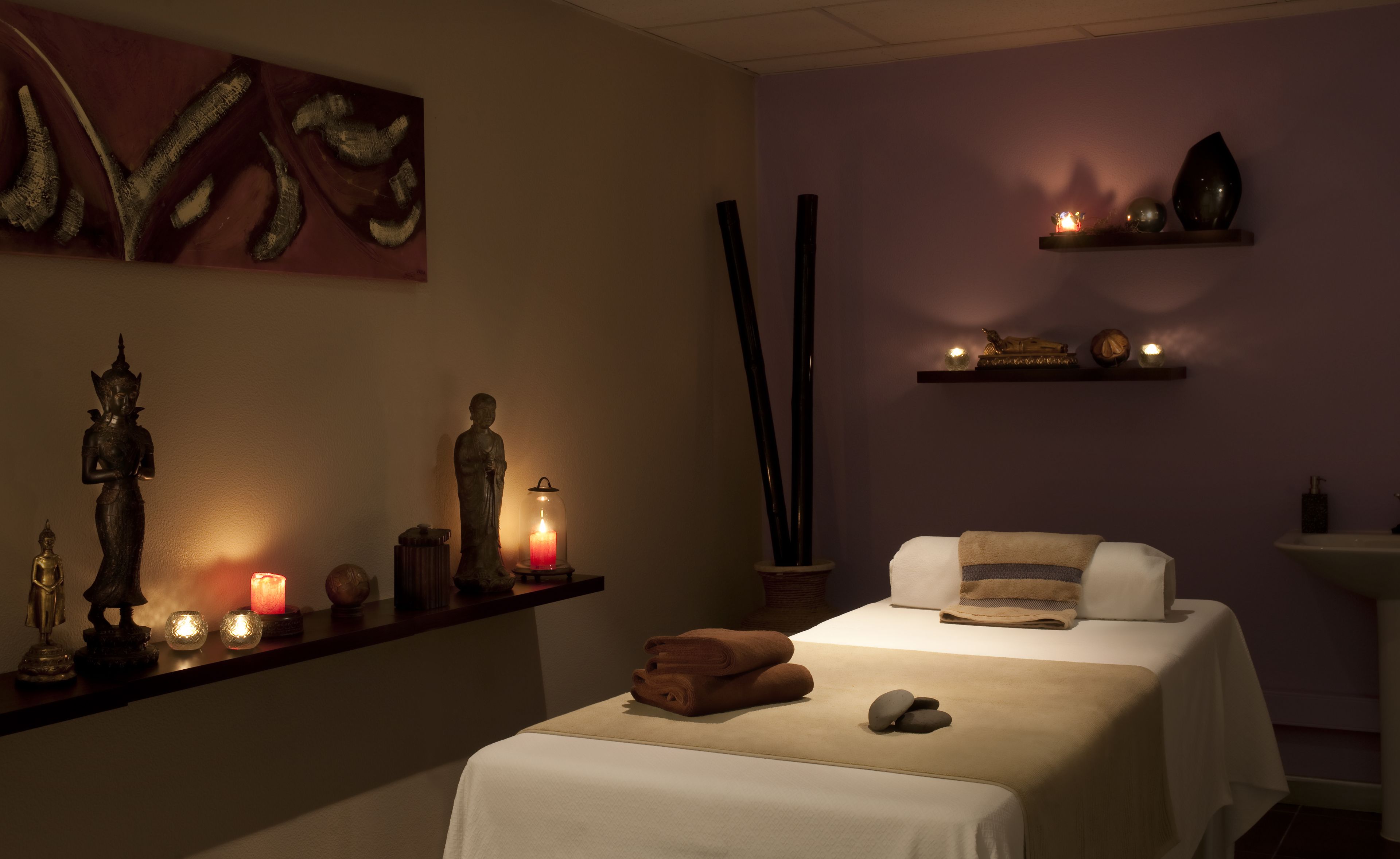 A spa room with a massage table, candles, and statues.
