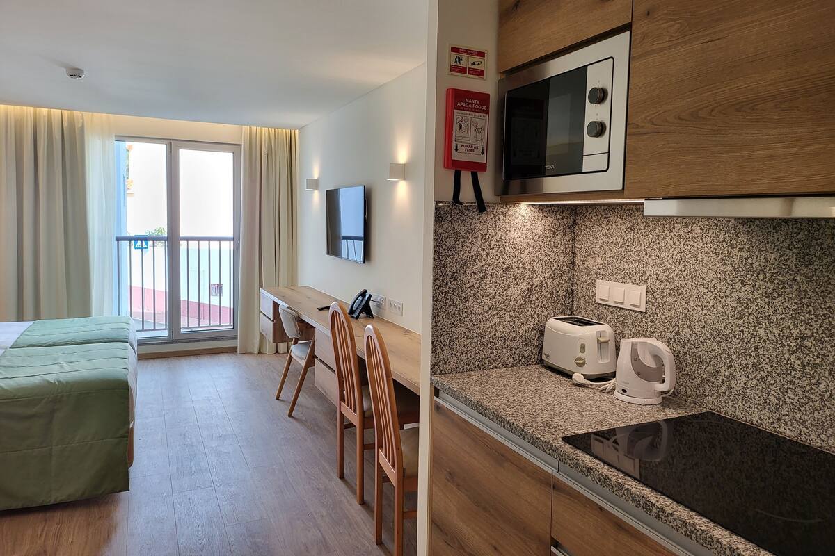 Ein Hotelzimmer mit Bett, Schreibtisch, Stuhl, Fernseher, Mikrowelle, Toaster und einer Küchenzeile.