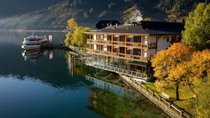 Un edificio frente a un lago, con un muelle, un bote y montañas al fondo.