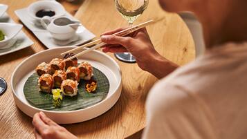 A person dining at a wooden table with a plate of sushi, a glass of white wine, and a cup of tea.