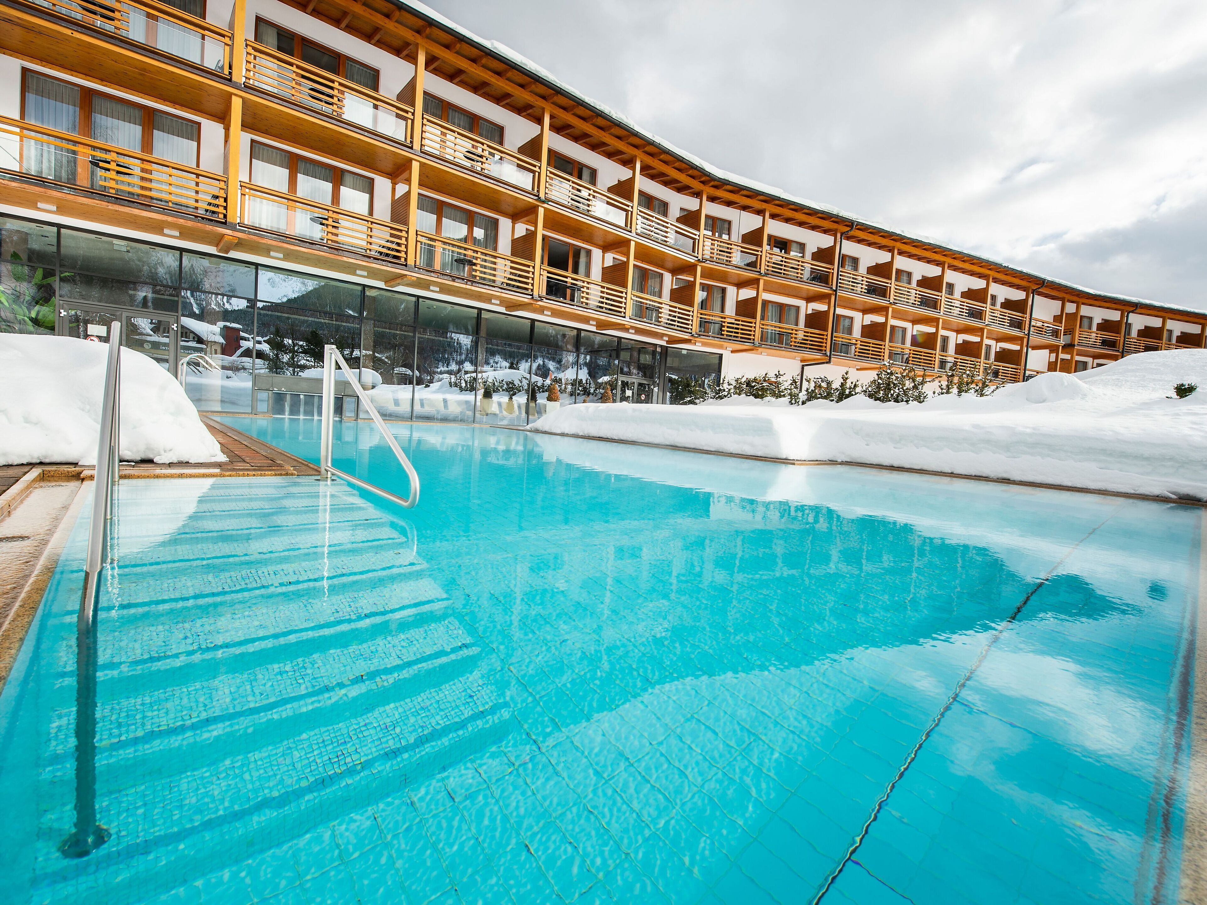 Ein Schwimmbecken mit hölzernen Balkonen und Blick auf verschneite Berge.