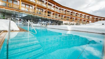 Ein Schwimmbecken mit hölzernen Balkonen und Blick auf verschneite Berge.