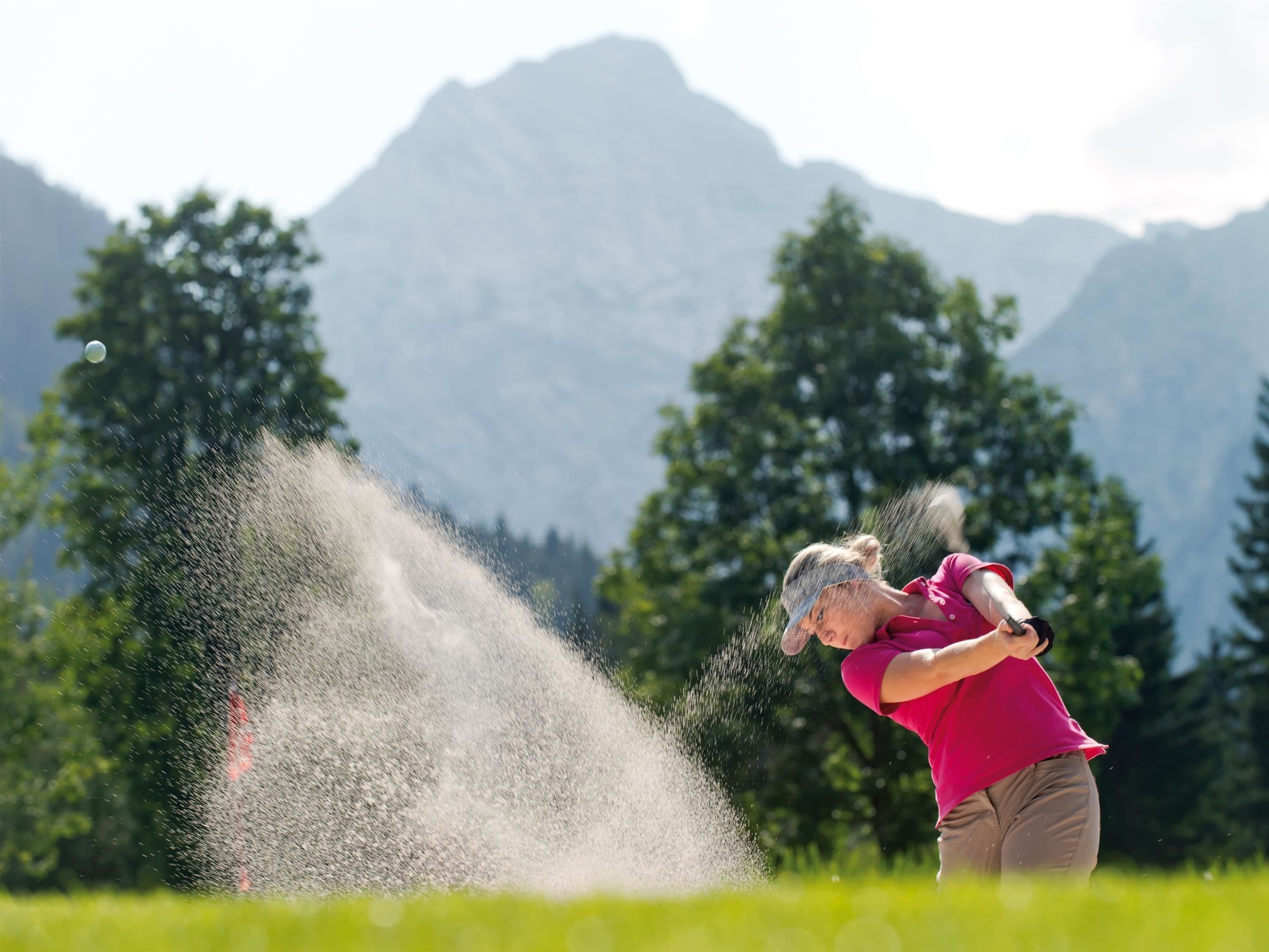 A person playing golf in a field with mountains in the background.