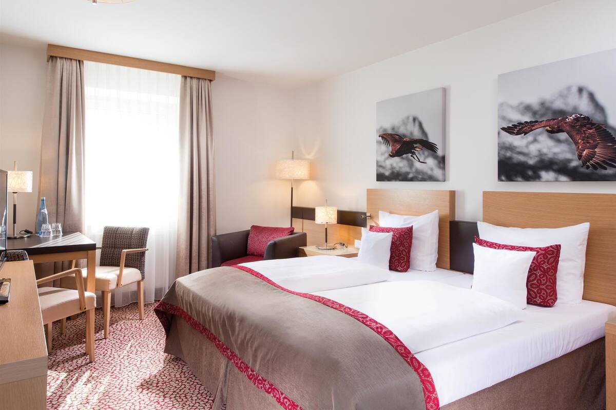Une chambre d’hôtel avec un grand lit, un bureau, une chaise et deux lampes fixées au mur.