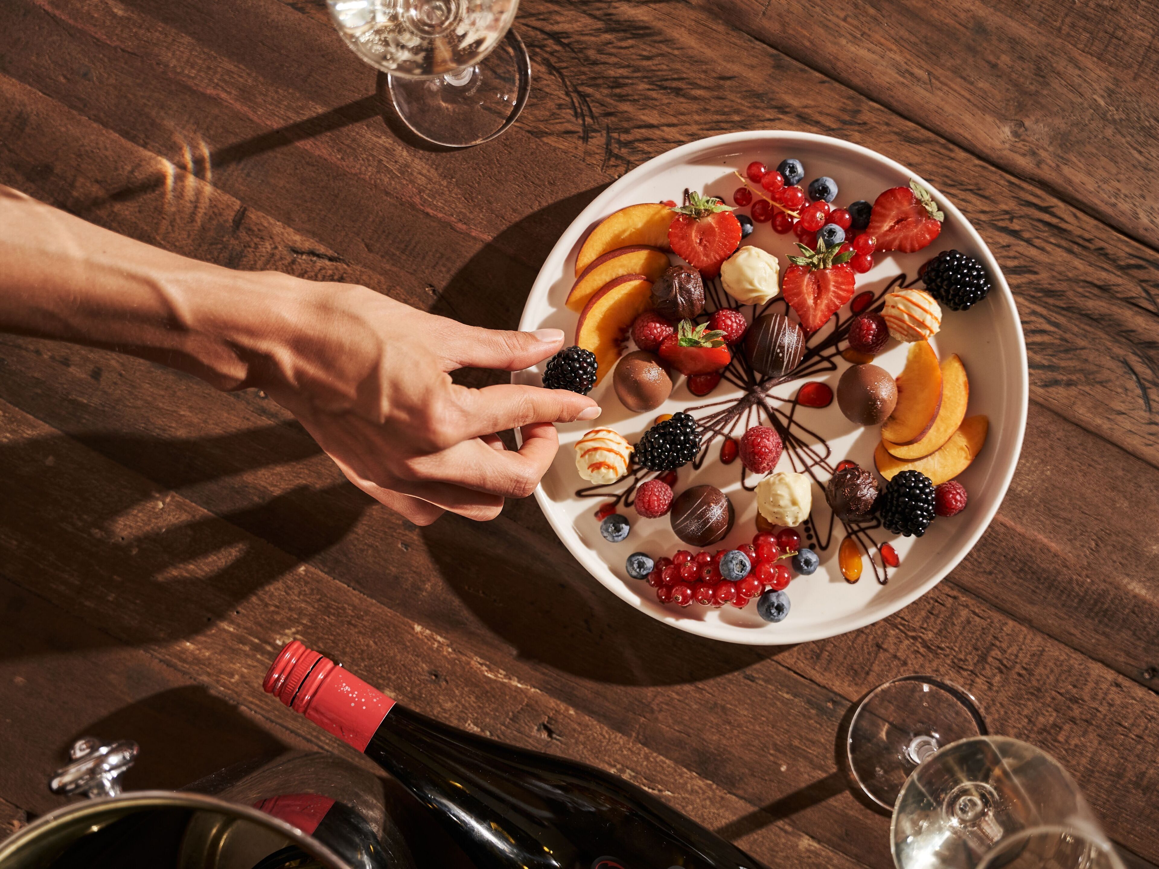 Une table en bois sur laquelle se trouve une assiette remplie de fruits variés et une bouteille de vin.
