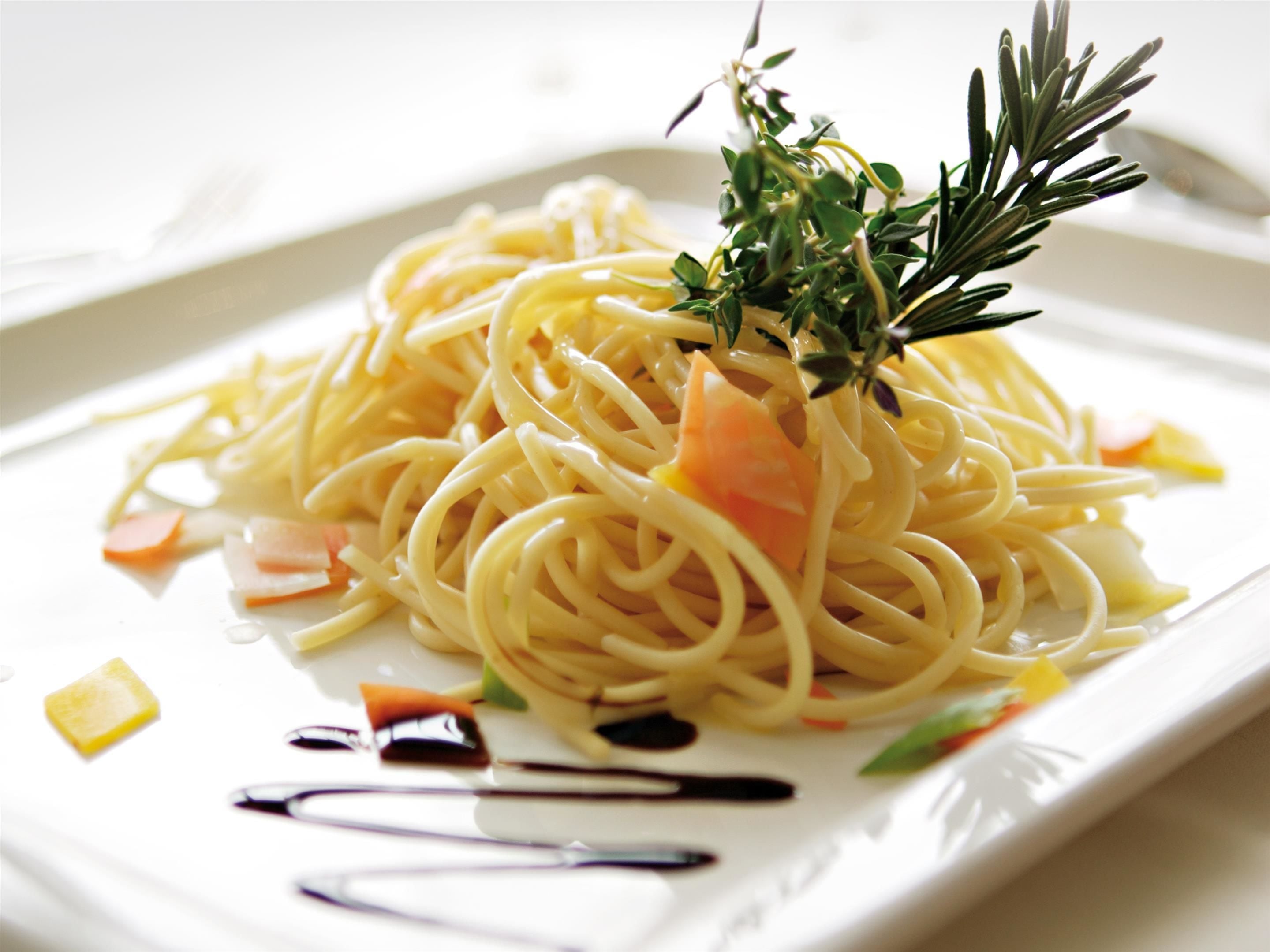 Un plato de espagueti con verduras y una ramita de romero.