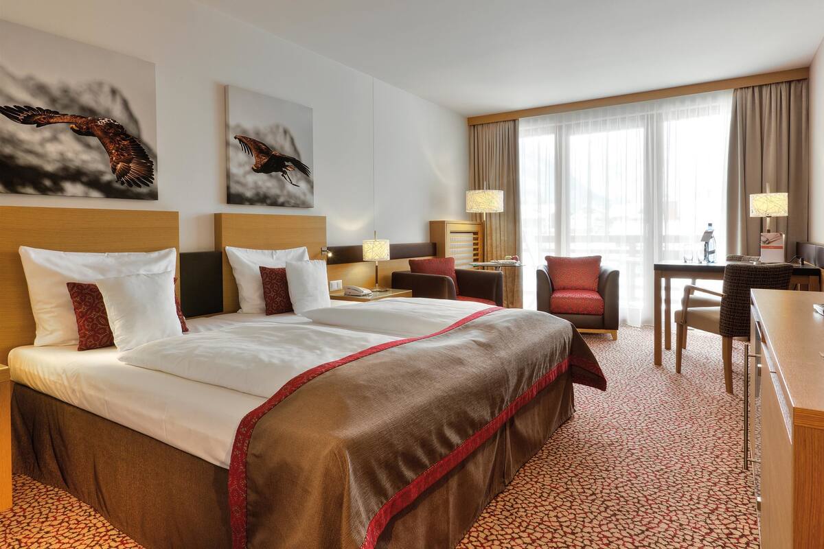 Une chambre d’hôtel avec un grand lit, un bureau, deux chaises, une lampe et des œuvres d’art accrochées aux murs.