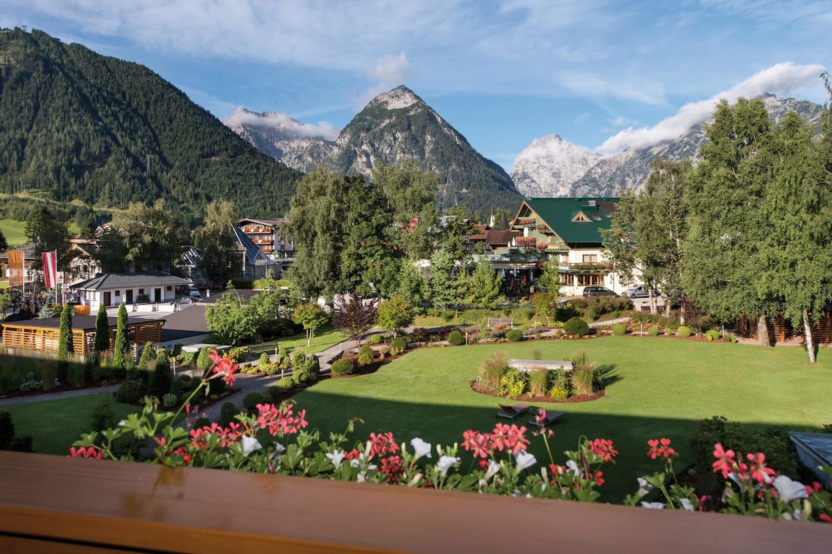 Un village de montagne à l’architecture traditionnelle, doté d’une grande pelouse centrale et offrant une vue sur des montagnes enneigées.