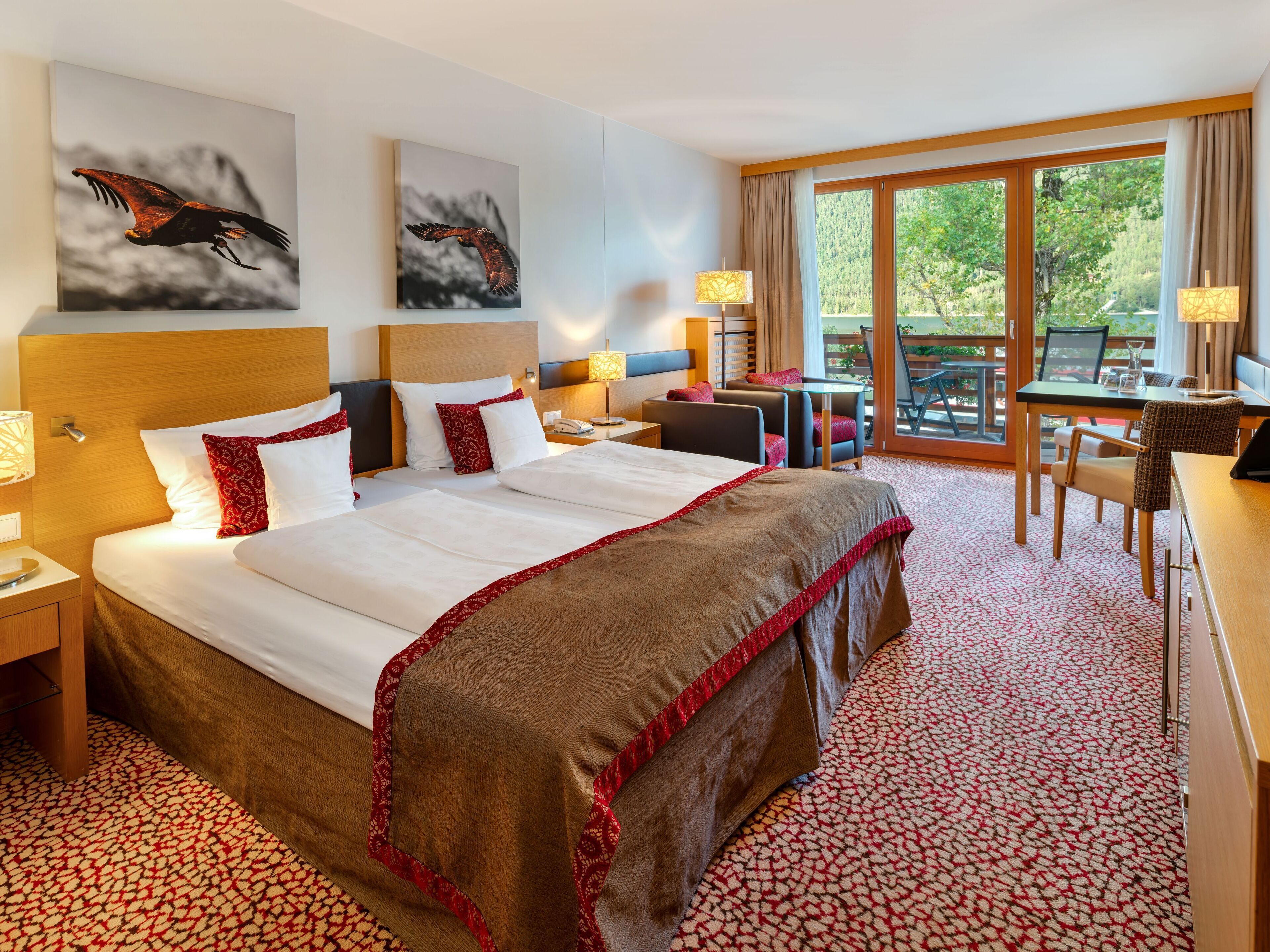 Une chambre d’hôtel avec un grand lit, un bureau et un balcon donnant sur la verdure.