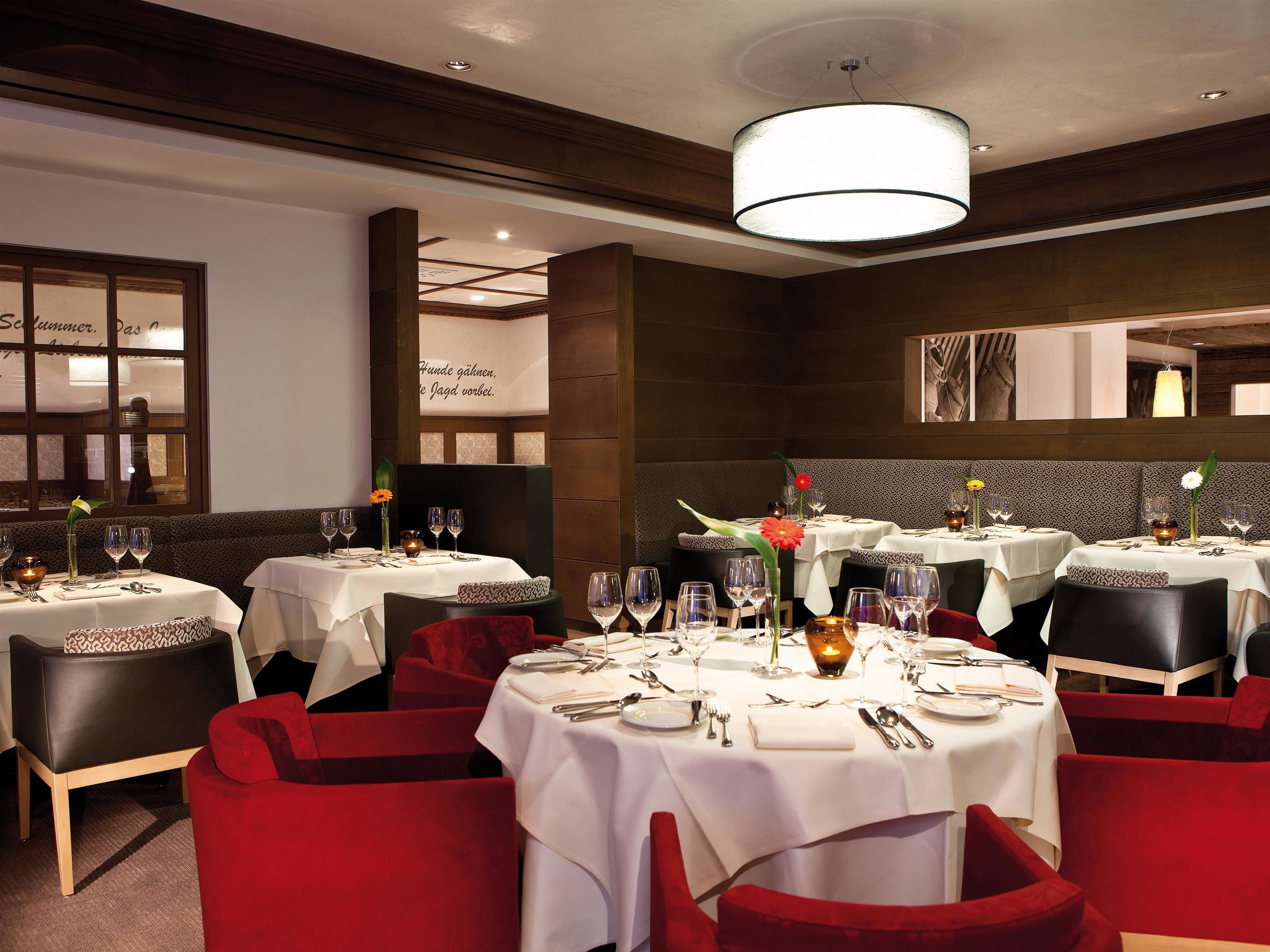 A restaurant with multiple tables set for dining, featuring white tablecloths and red upholstered chairs.