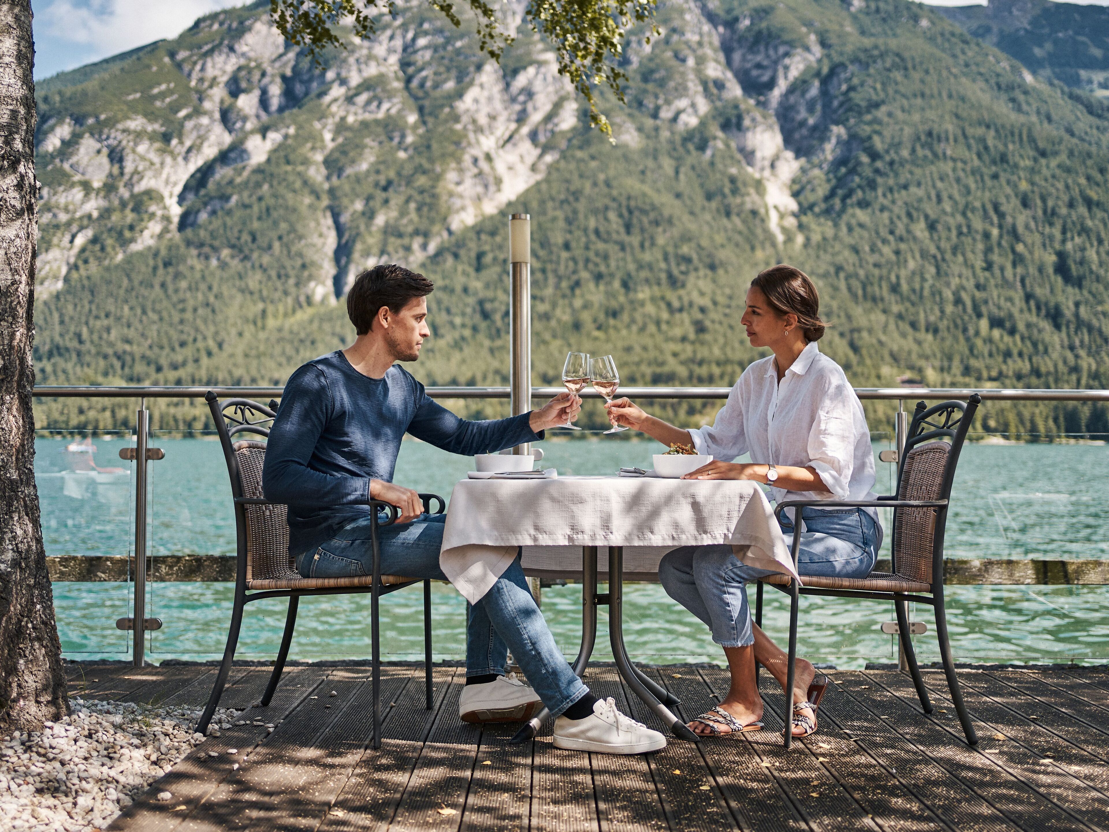 Two people seated at a table with a view of a lake and mountains in the background.