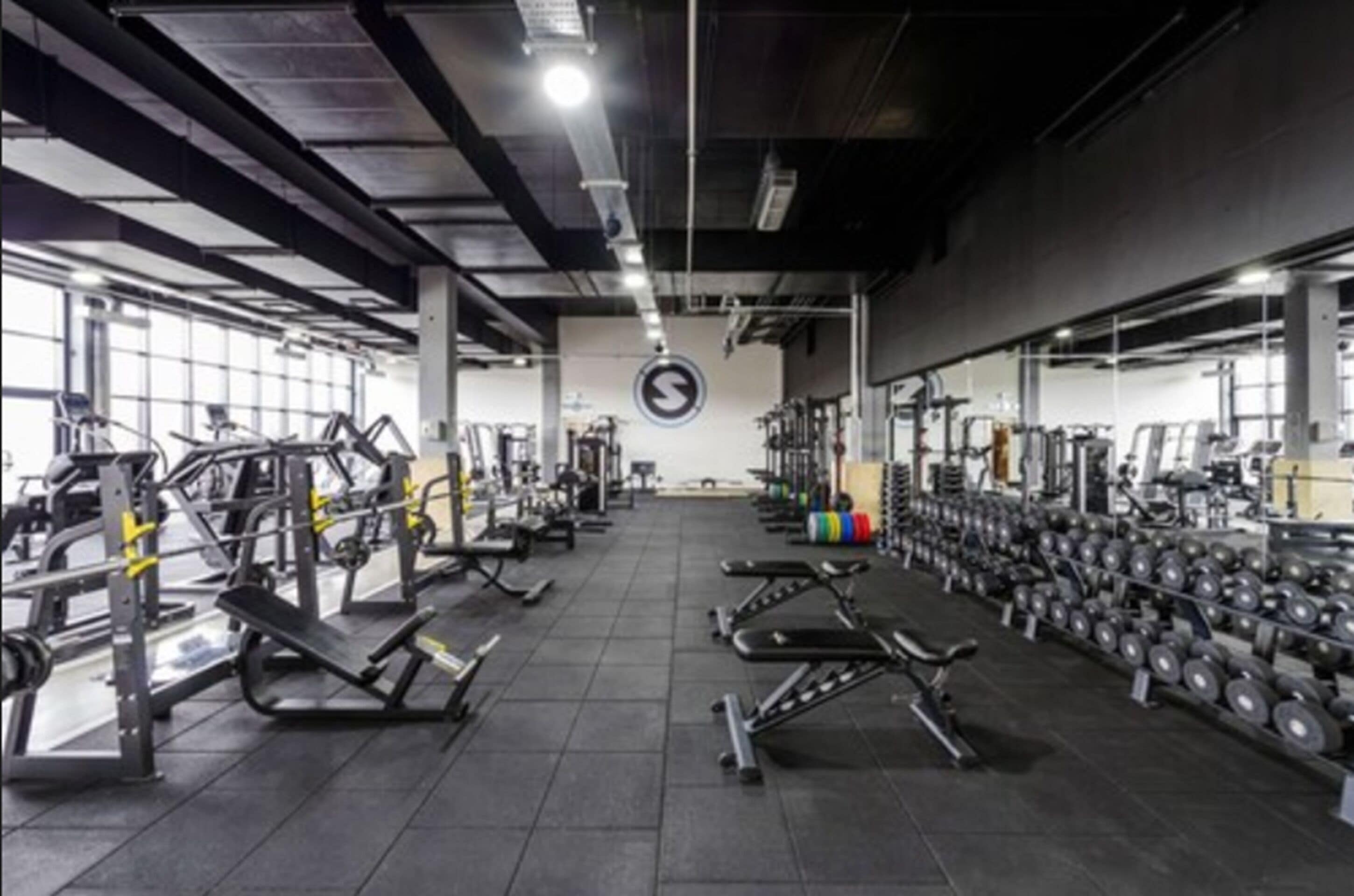 Un gimnasio con varios equipos de ejercicio, incluyendo máquinas de pesas y mancuernas, dispuestos en filas.