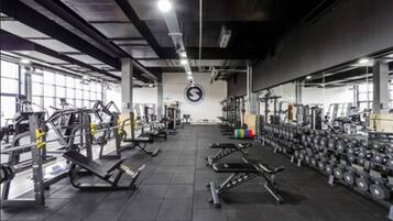 Un gimnasio con varios equipos de ejercicio, incluyendo máquinas de pesas y mancuernas, dispuestos en filas.