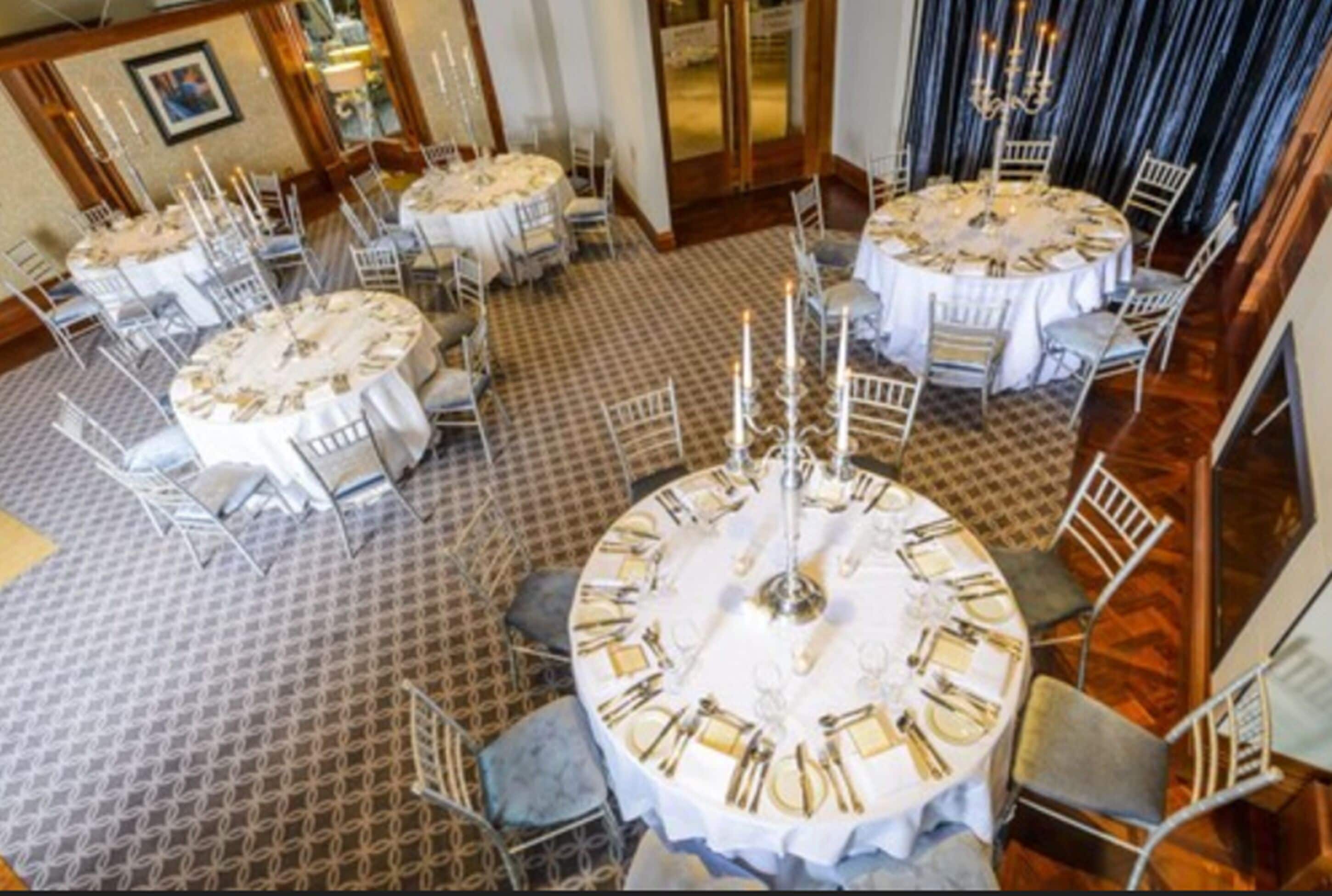 Comedor con mesas redondas dispuestas para varios invitados, con manteles blancos y cubertería dorada.