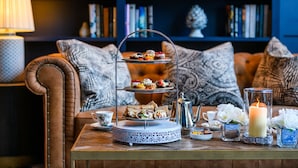 A three-tiered dessert stand with various pastries on a wooden table, surrounded by decorative items and a bookshelf in the background. - Shearwater Hotel & Spa (Ballinasloe)