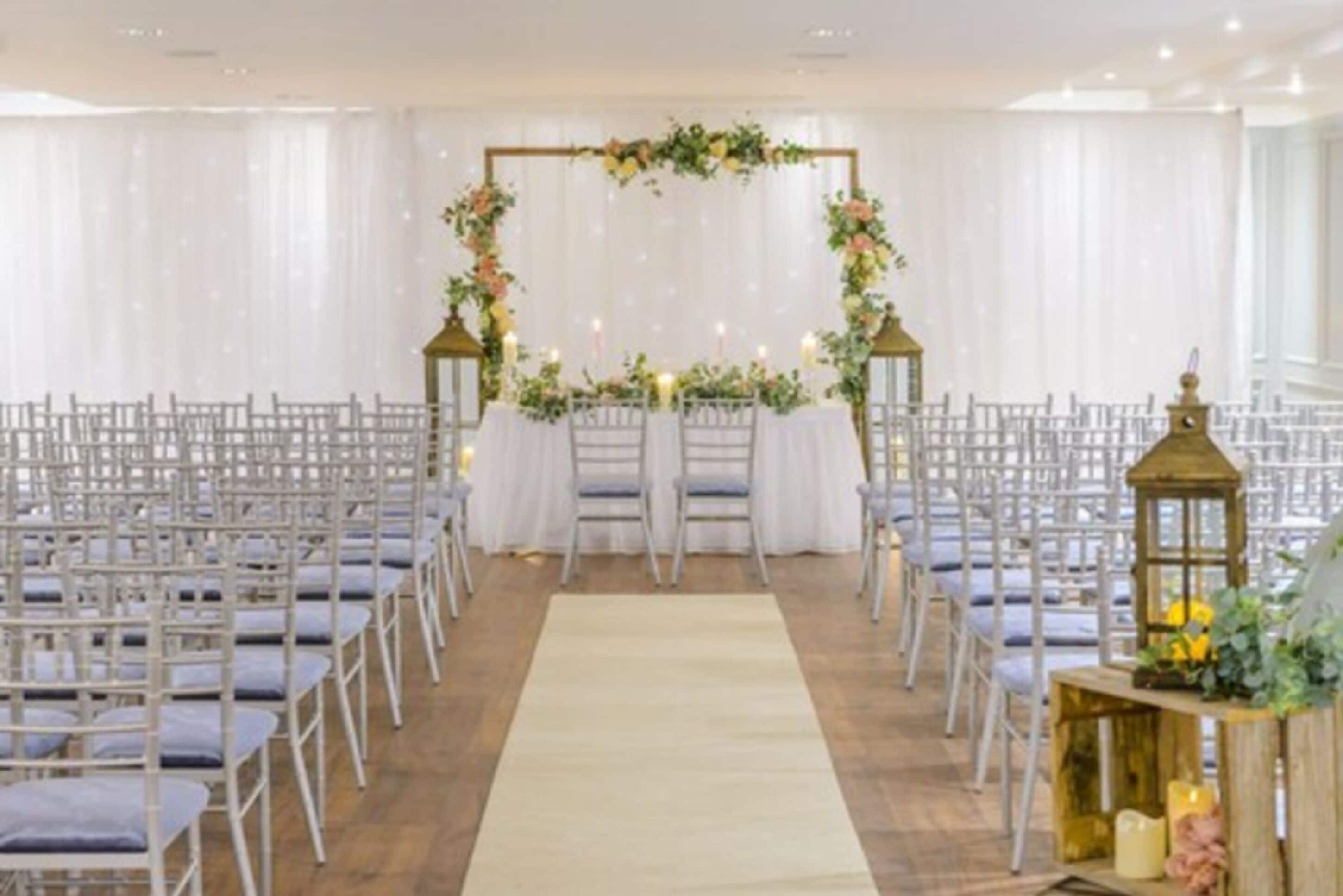 A wedding ceremony aisle with white chairs and a floral arch.