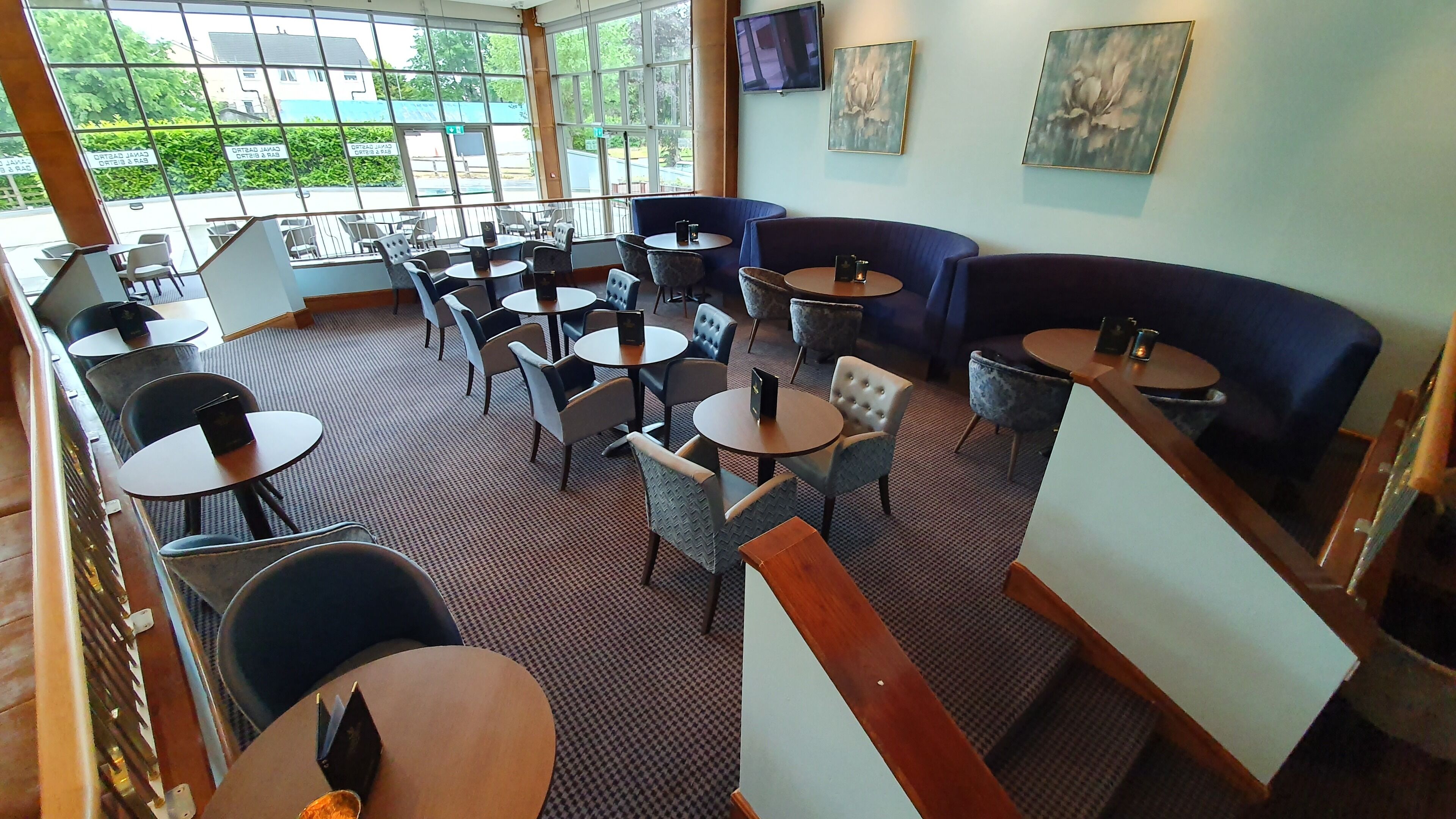 A restaurant with round tables and chairs, a large window with a view, and artwork on the walls.