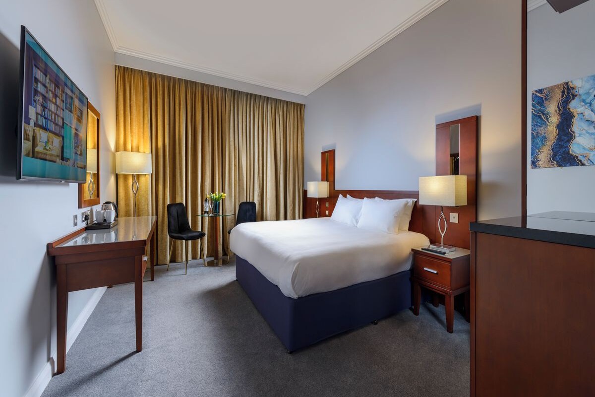 Habitación de hotel con una cama grande, un escritorio, una silla, un televisor y una ventana con cortinas.