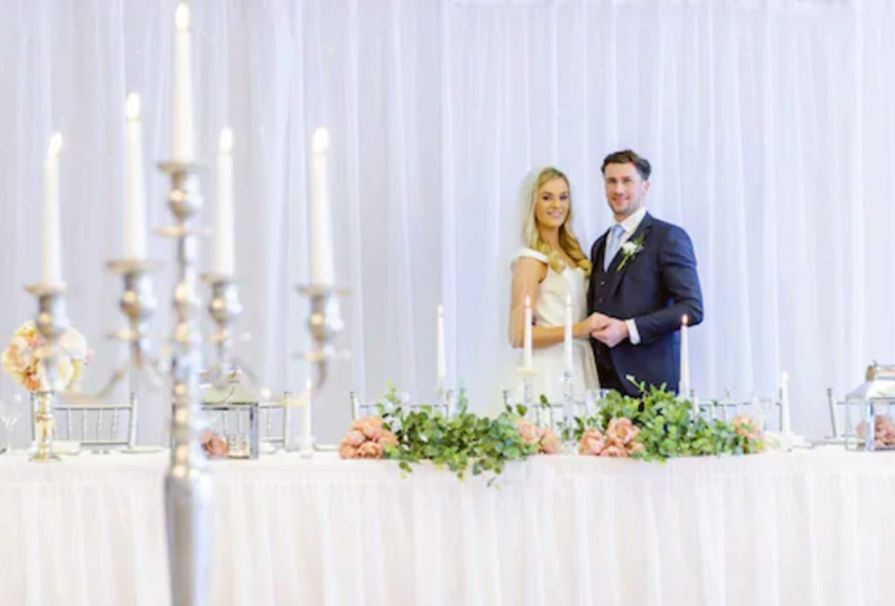 A wedding reception with a white table set with candles and floral arrangements.