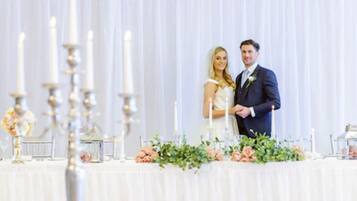 A wedding reception with a white table set with candles and floral arrangements.
