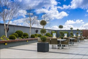 An outdoor patio area with tables and chairs, surrounded by neatly trimmed hedges and trees. - Shearwater Hotel & Spa (Ballinasloe)