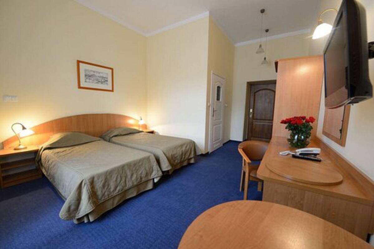 A hotel room with two beds, a desk with a chair, a TV, and a door.
