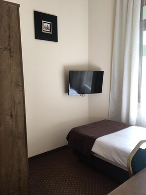 A hotel room with a bed, a television mounted on the wall, a framed picture, and a window with curtains. - Hotel Matejko (Kraków)