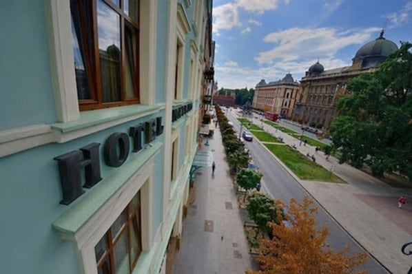 A hotel with a prominent 'HOTEL' sign on the facade, a pedestrian walkway, and a street with trees and buildings in the background.