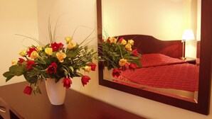 Quarto de hotel com cama, mesa de cabeceira com luminária e espelho refletindo o aposento.