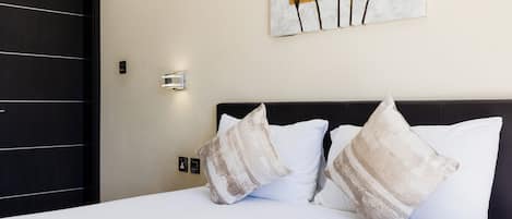 Una habitación de hotel con una cama, dos almohadas decorativas, una obra de arte en la pared y una puerta.
