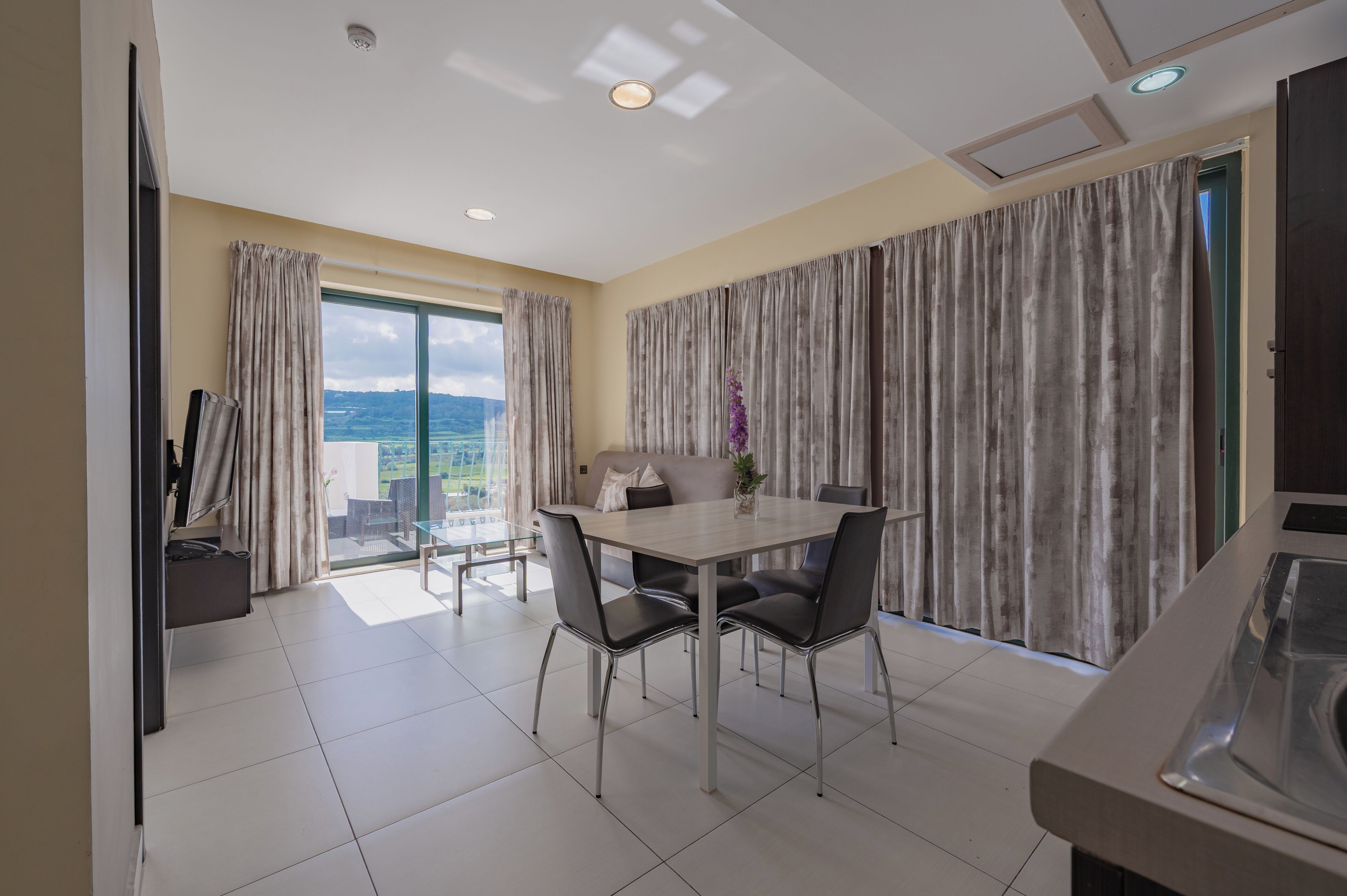 Un moderno comedor con mesa y sillas, ventanas amplias con cortinas, y vista al exterior.