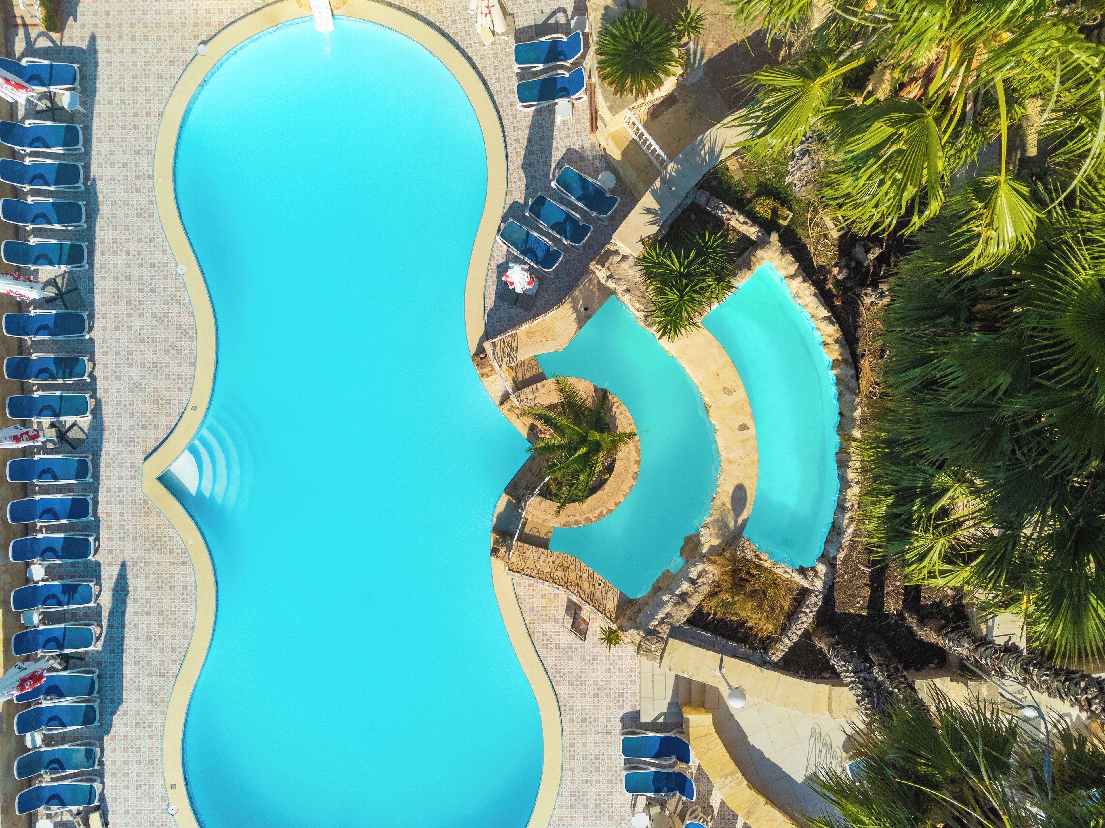 A large, clear blue pool with multiple lounge chairs and palm trees around it.