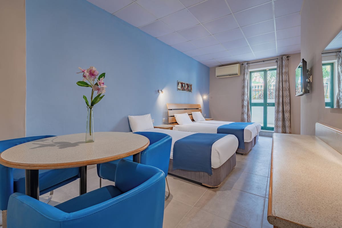 Een hotelkamer met een bed, een tafeltje, blauwe stoelen en een vaas met bloemen.