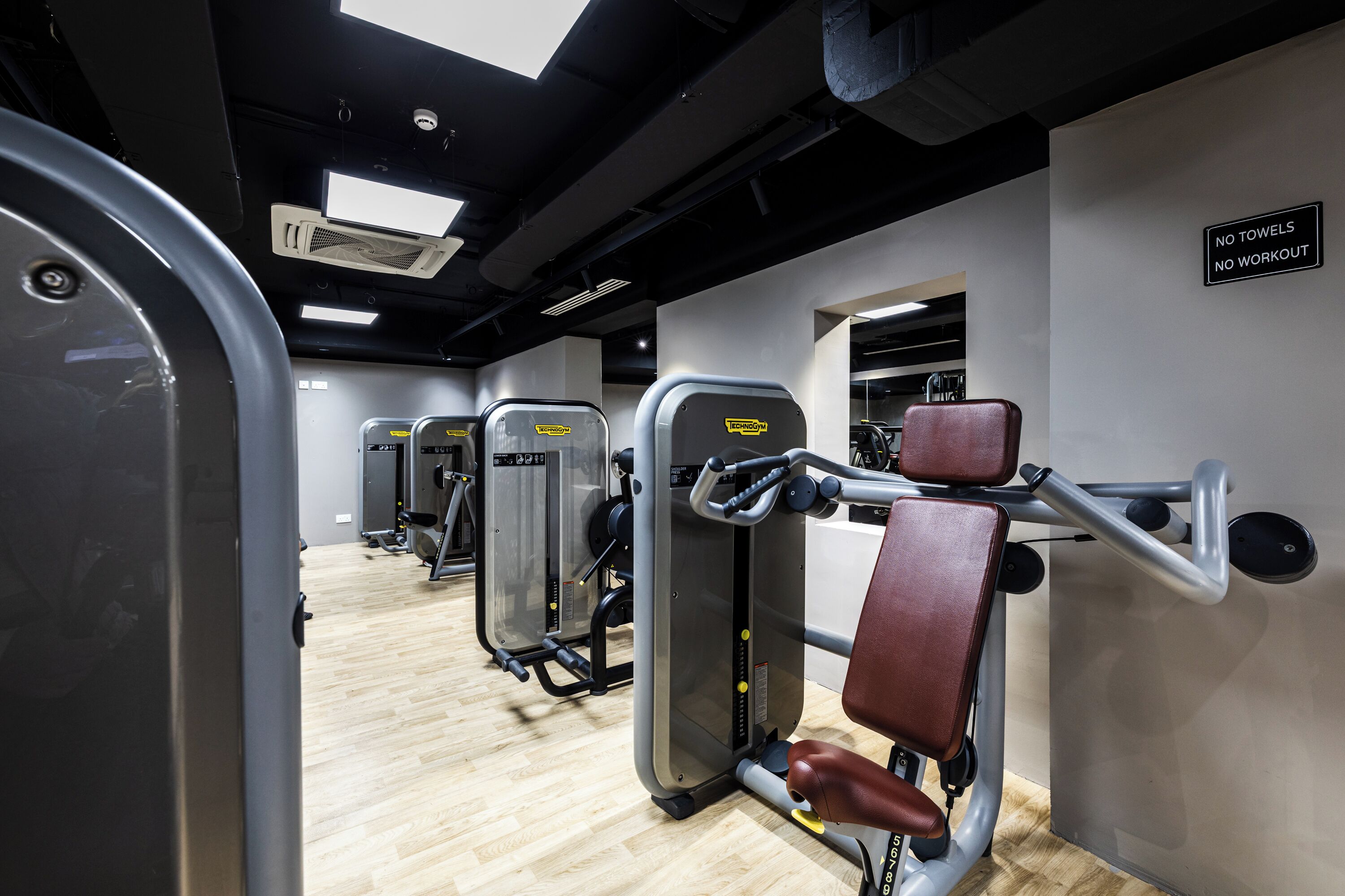 Un gimnasio con máquinas de ejercicio, un cartel que prohíbe el uso de toallas y suelo de madera.